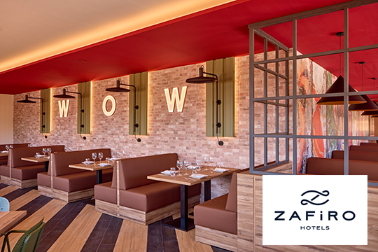 Bar mit braunen Tischen und Stühlen, an der Wand die Leuchtschrift WOW